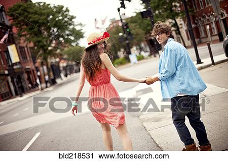 Stock Image - Rear view of couple walking on city sidewalk. Fotosearch
