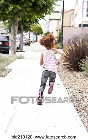 Stock Image - Rear view of girl running on city sidewalk. Fotosearch