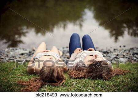 Stock Image - Rear view of girls laying near lake. Fotosearch
