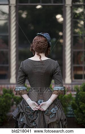 Stock Image - Rear view of woman wearing vintage gown and hat. Fotosearch