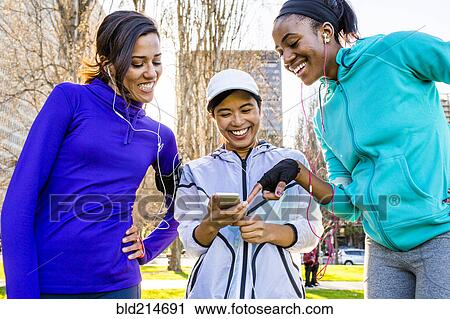 Stock Image - Runners using cell phone in urban park. Fotosearch