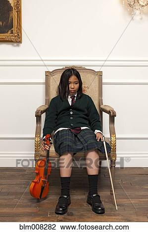 Stock Image - Sad Vietnamese girl sitting in elegant chair holding violin. Fotosearch