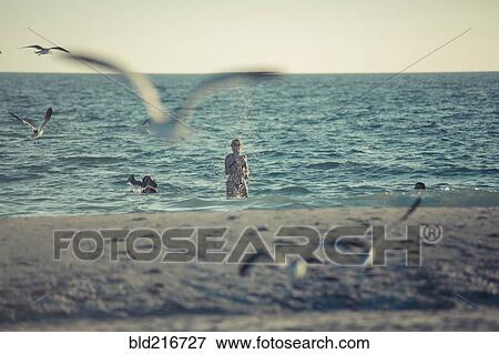 Stock Photo - Seagulls flying near Caucasian teenage girl standing in ocean. Fotosearch