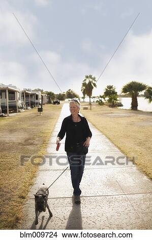 Picture - Senior Caucasian woman walking dog on sidewalk. Fotosearch