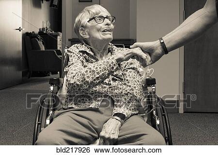 Stock Photograph - Senior woman in wheelchair shaking hand of man. Fotosearch