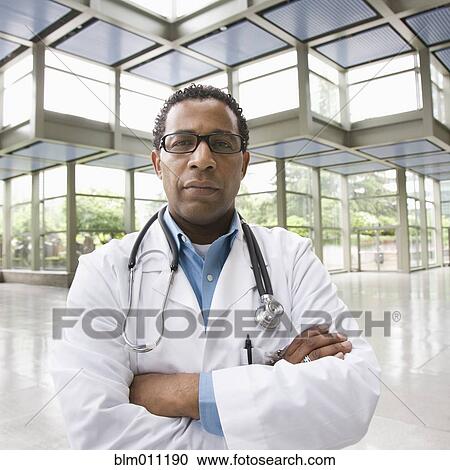Stock Image - Serious African American doctor standing in lobby. Fotosearch