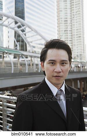 Stock Image - Serious Asian businessman standing outdoors. Fotosearch