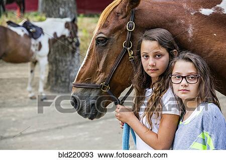 Stock Image - Serious girls leading horse on ranch. Fotosearch