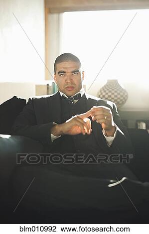 Stock Image - Serious mixed race businessman sitting in chair. Fotosearch