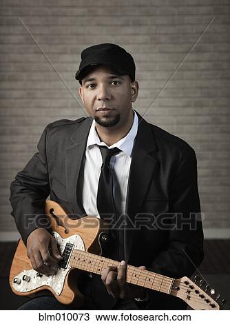 Stock Image - Serious mixed race man holding electric guitar. Fotosearch