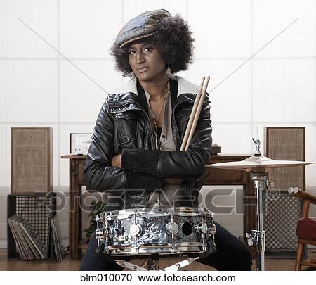 Stock Image - Serious mixed race woman sitting with drums. Fotosearch