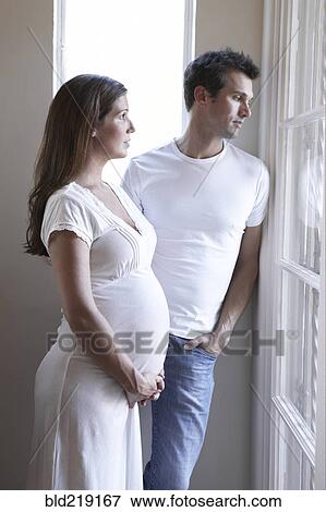 Stock Photo - Serious pregnant couple looking out window. Fotosearch