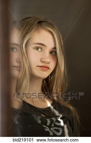 Stock Image - Serious teenage girl examining herself in mirror. Fotosearch