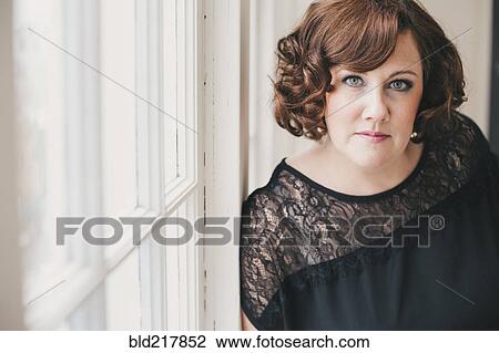 Stock Image - Serious woman leaning on window. Fotosearch