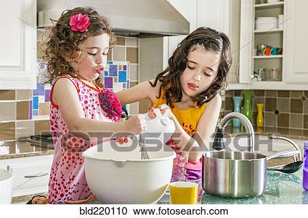 Stock Image - Sisters baking in kitchen. Fotosearch
