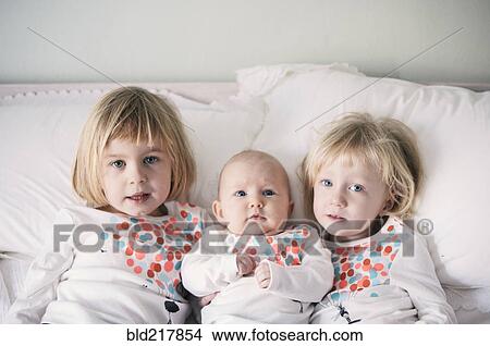 Picture - Sisters in matching shirts laying on bed. Fotosearch
