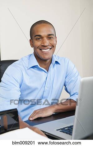 Smiling African American businessman sitting at desk View Large Photo Image Stock Image - Smiling African American businessman sitting at desk. Fotosearch