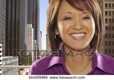 Stock Photography - Smiling Asian businesswoman with city in background. Fotosearch