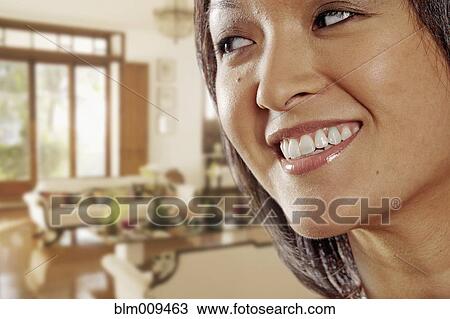 Stock Image - Smiling Asian woman in living room. Fotosearch