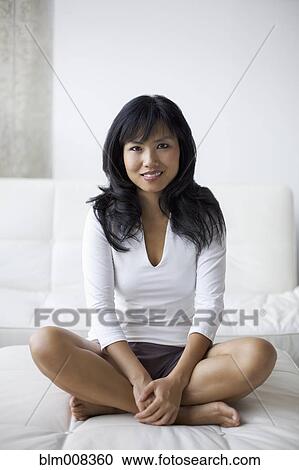 Stock Image - Smiling Asian woman sitting in living room. Fotosearch