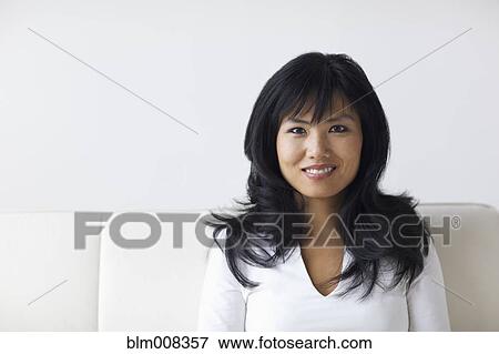 Smiling Asian woman sitting on sofa View Large Photo Image Stock Photo - Smiling Asian woman sitting on sofa. Fotosearch