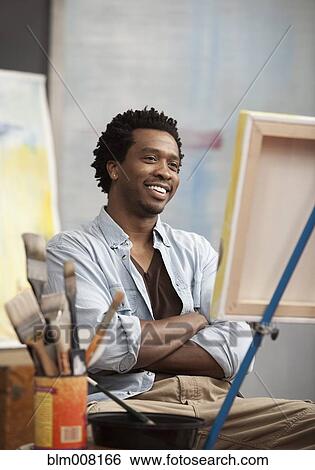 Stock Photograph - Smiling Black artist looking at easel. Fotosearch