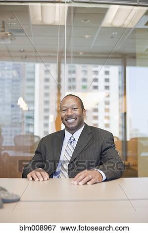 Smiling Black businessman sitting in conference room View Large Photo Image Stock Photo - Smiling Black businessman sitting in conference room. Fotosearch