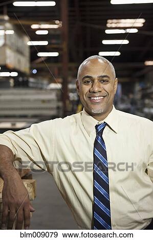 Stock Photo - Smiling Black manager standing in factory. Fotosearch