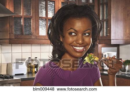 Smiling Black woman eating salad in kitchen View Large Photo Image Stock Photo - Smiling Black woman eating salad in kitchen. Fotosearch