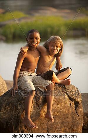 Picture - Smiling boys hugging on rock near lake. Fotosearch
