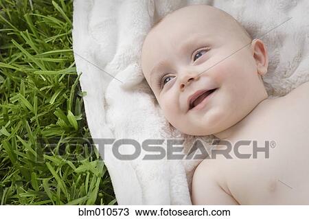 Stock Image - Smiling Caucasian baby laying in grass. Fotosearch