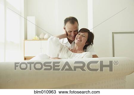 Smiling Caucasian couple sitting together on sofa View Large Photo Image Stock Image - Smiling Caucasian couple sitting together on sofa. Fotosearch