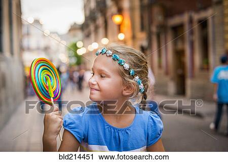 Stock Image - Smiling Caucasian girl enjoying lollipop in city. Fotosearch