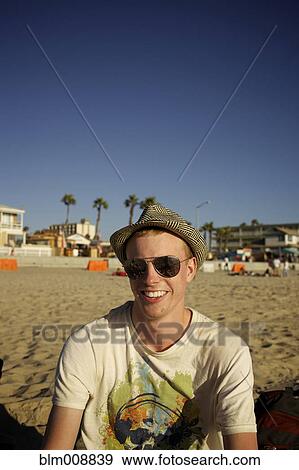 Stock Photo - Smiling Caucasian man sitting on beach. Fotosearch