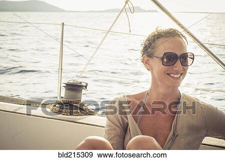 Stock Photo - Smiling Caucasian woman sitting on boat deck. Fotosearch