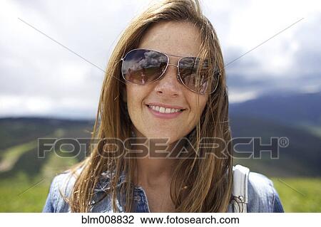 Stock Image - Smiling Caucasian woman wearing sunglasses outdoors. Fotosearch