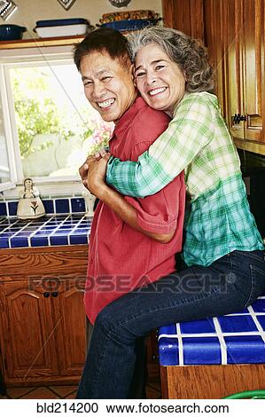 Stock Image - Smiling couple hugging in kitchen. Fotosearch