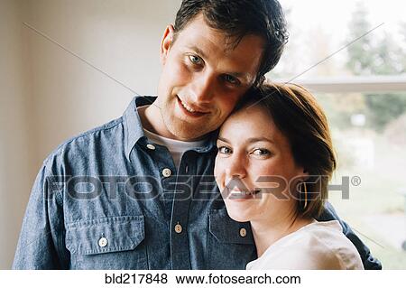 Smiling couple hugging near window View Large Photo Image Stock Photo - Smiling couple hugging near window. Fotosearch