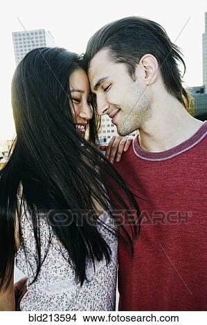 Picture - Smiling couple hugging on urban rooftop. Fotosearch