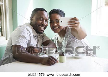 Smiling couple taking cell phone selfie at table View Large Photo Image Stock Photograph - Smiling couple taking cell phone selfie at table. Fotosearch
