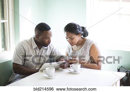 Stock Photograph - Smiling couple using cell phone and digital tablet at breakfast. Fotosearch