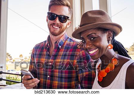 Stock Image - Smiling couple using cell phone together. Fotosearch