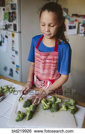 Stock Photograph - Smiling girl chopping broccoli in kitchen. Fotosearch