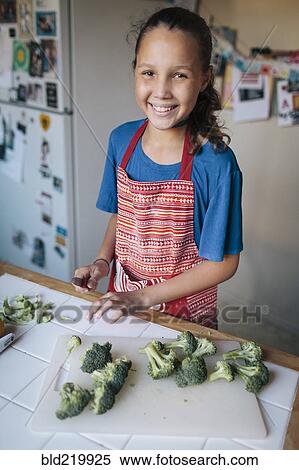Stock Photography - Smiling girl chopping broccoli in kitchen. Fotosearch