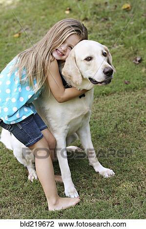 Stock Image - Smiling girl hugging dog in field. Fotosearch