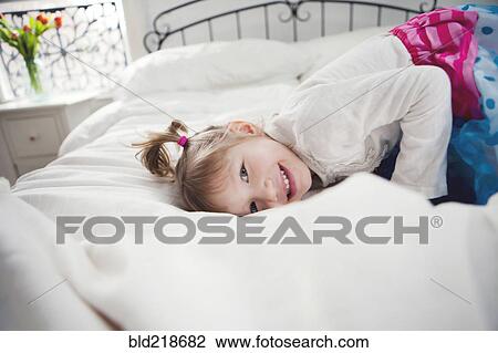 Stock Image - Smiling girl playing on bed. Fotosearch