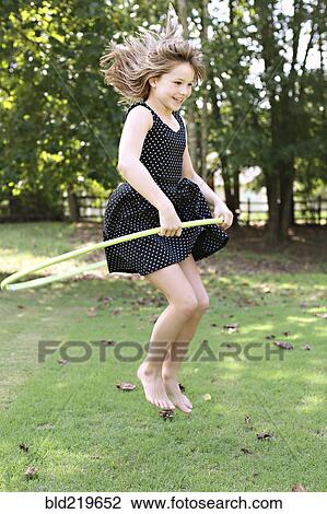 Stock Image - Smiling girl playing with plastic hoop in field. Fotosearch