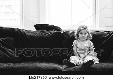 Stock Image - Smiling girl sitting on sofa. Fotosearch
