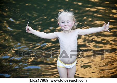 Stock Photo - Smiling girl standing with arms outstretched at lake. Fotosearch