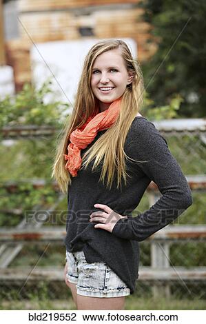 Stock Image - Smiling girl standing with hands on hips outdoors. Fotosearch